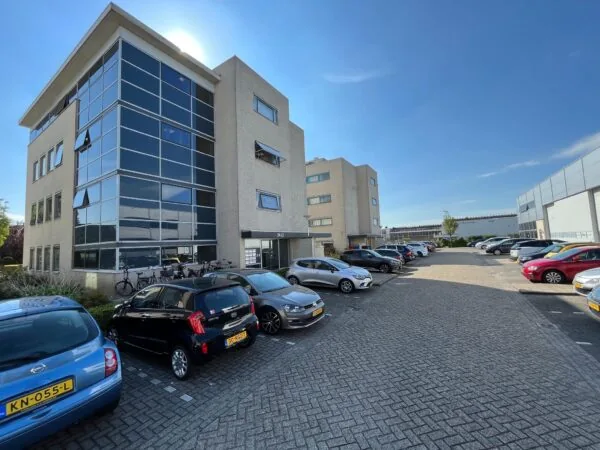 Bedrijventerrein in Leidse Rijn met kantoorpand, geparkeerde auto’s en fietsen onder een blauwe lucht.